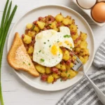 Finished Corned Beef Hash with crispy potatoes, tender corned beef, and a fried egg on top, garnished with fresh green onions.
