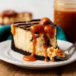 A slice of Turtle Cheesecake on a dessert plate with visible layers of chocolate crust, creamy cheesecake filling, and caramel-pecan topping.
