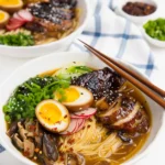 Bowl of Ginger Glazed Chicken Ramen with sliced soy chicken, ramen egg, greens, mushrooms, and scallions.