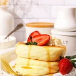 Fluffy Japanese soufflé pancakes stacked high with whipped cream and berries